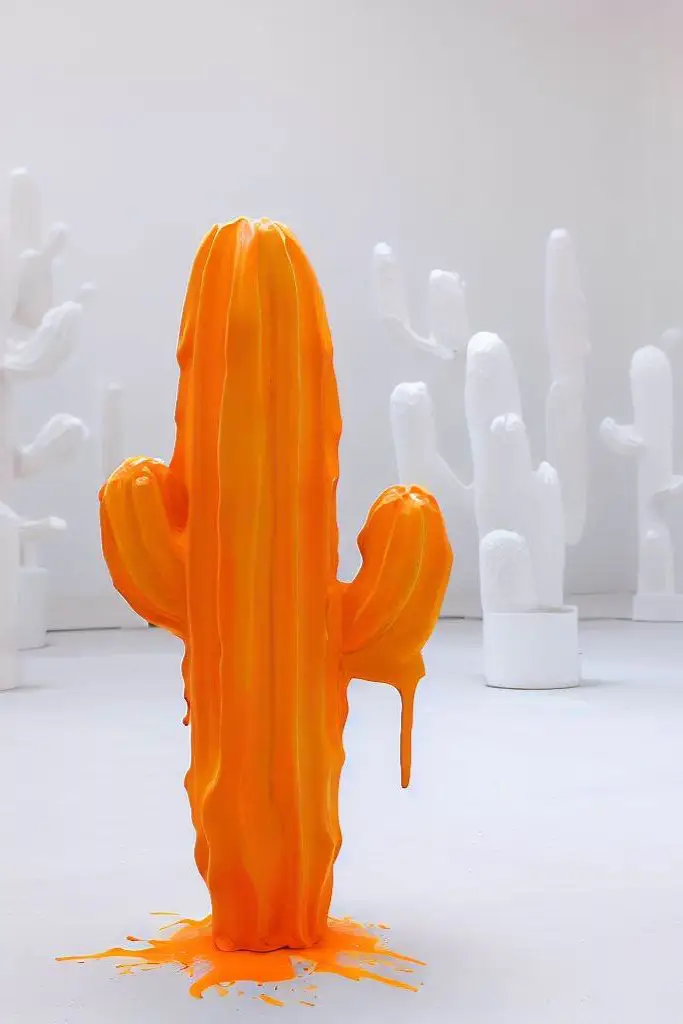 A cactus statue with orange paint and another classic white statue in the background (Generated with @dall-e)